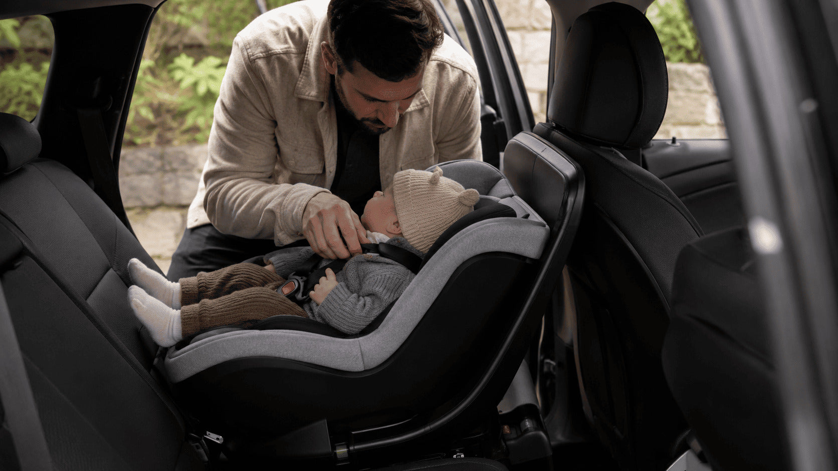 Parent fastening a baby into a rear-facing infant car seat with an ISOFIX base in the back of a family car.