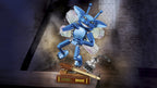 A blue robotic insect figure with translucent wings stands on a wooden surface in a dimly lit room, with a small book, a wooden rod, and a glass bottle nearby.