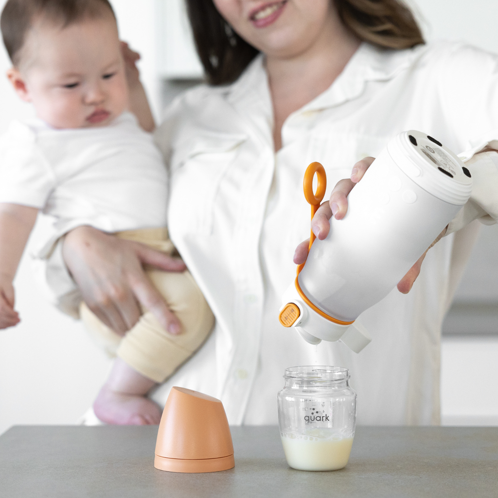 Person using a baby bottle warmer with a baby sitting next to them