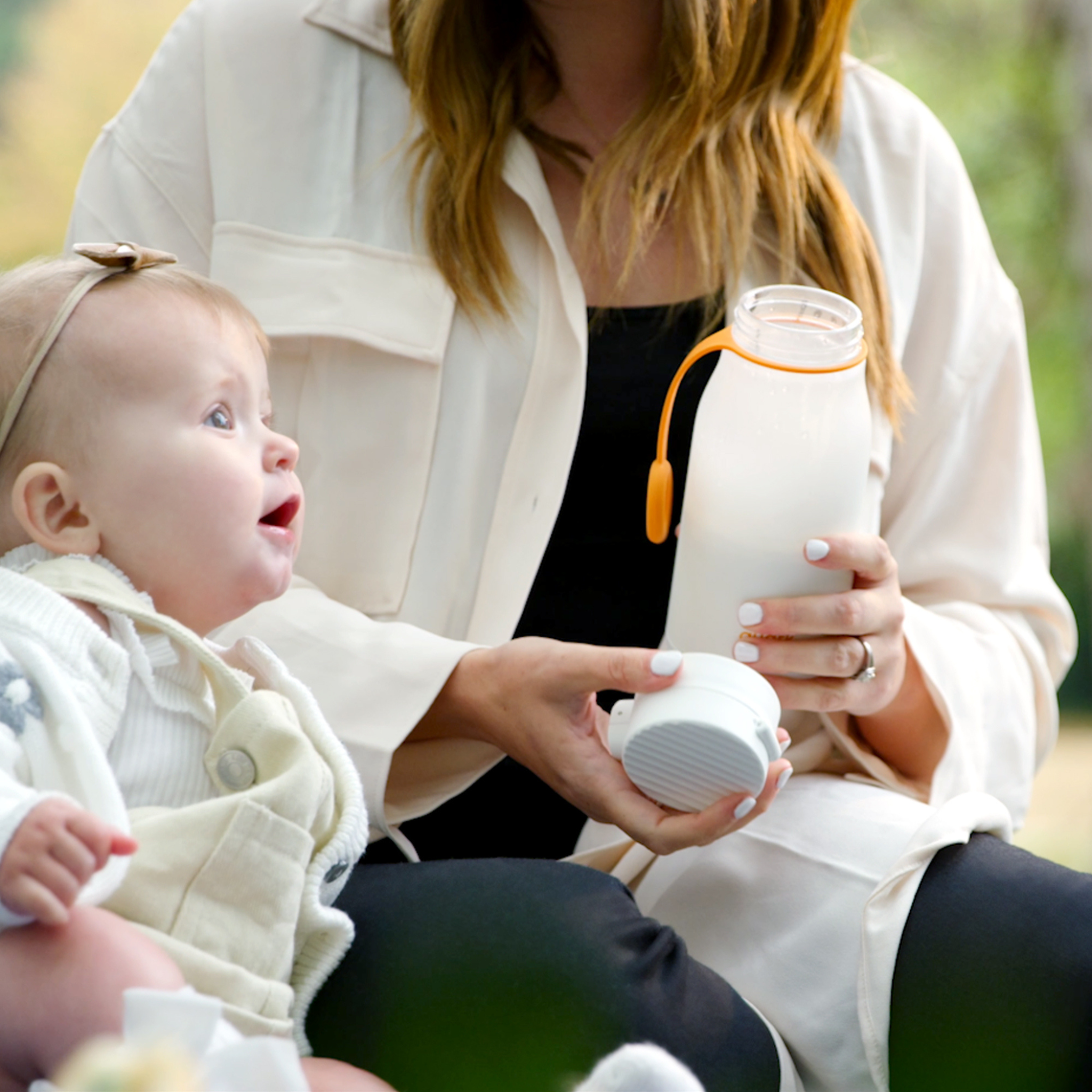 Woman holding a glass bottle with a baby outdoors