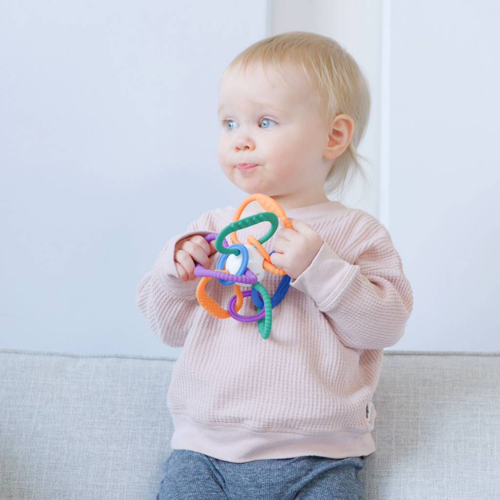 Child holding a colorful teething ring against a light background