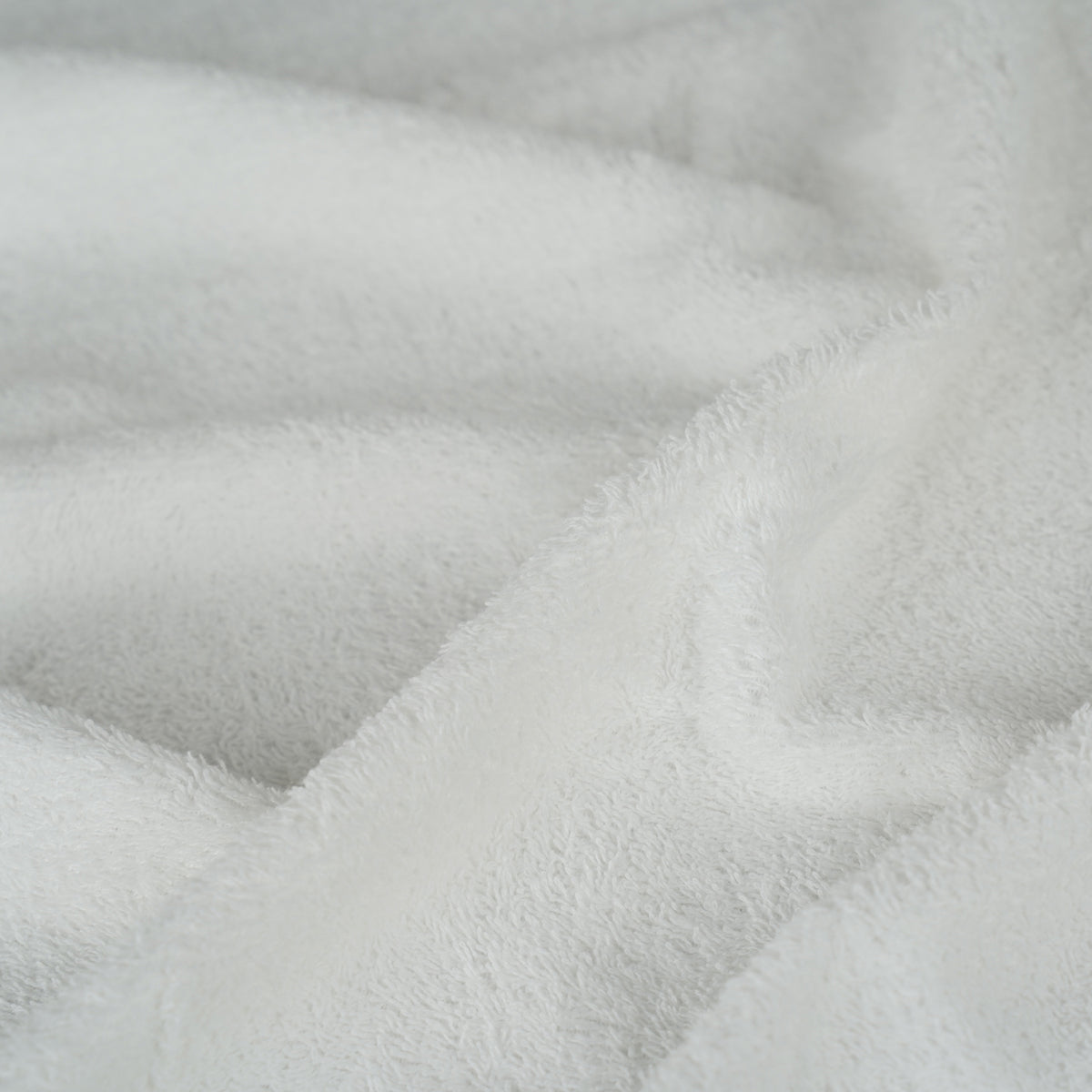 A close-up of soft white plush fabric with a textured, terry-like surface and gentle folds.