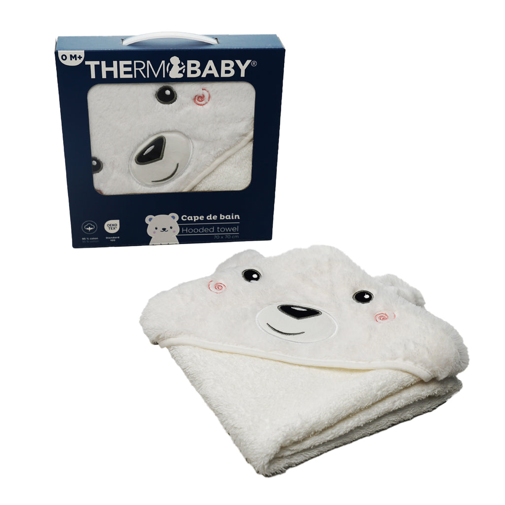 A white plush baby hooded towel with a bear face design is shown in front of its navy blue Thermobaby retail box on a plain white background.