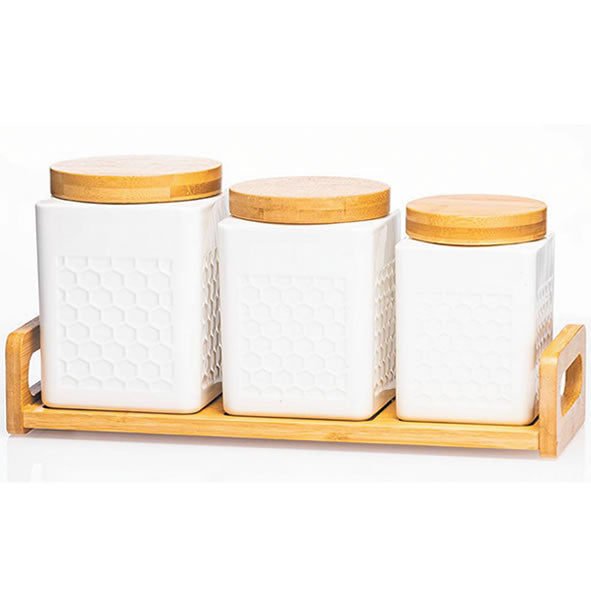 A set of three white ceramic cannisters with geometric patterns on the lids, placed on a wooden tray.