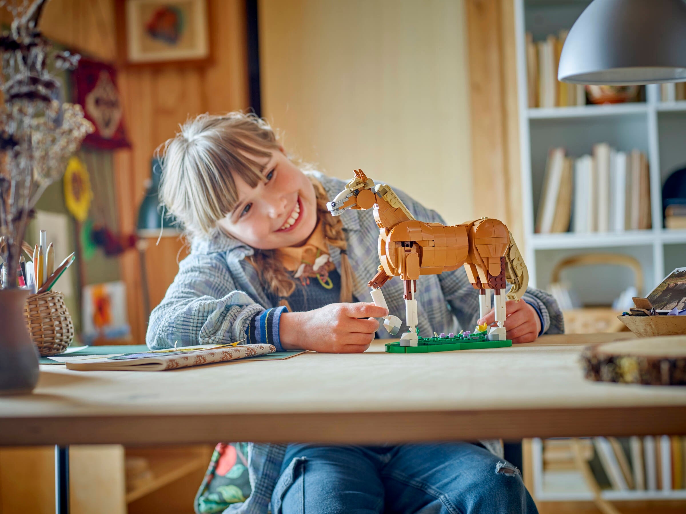 Child playing with a wooden horse toy at a table in a room with books and decor.
