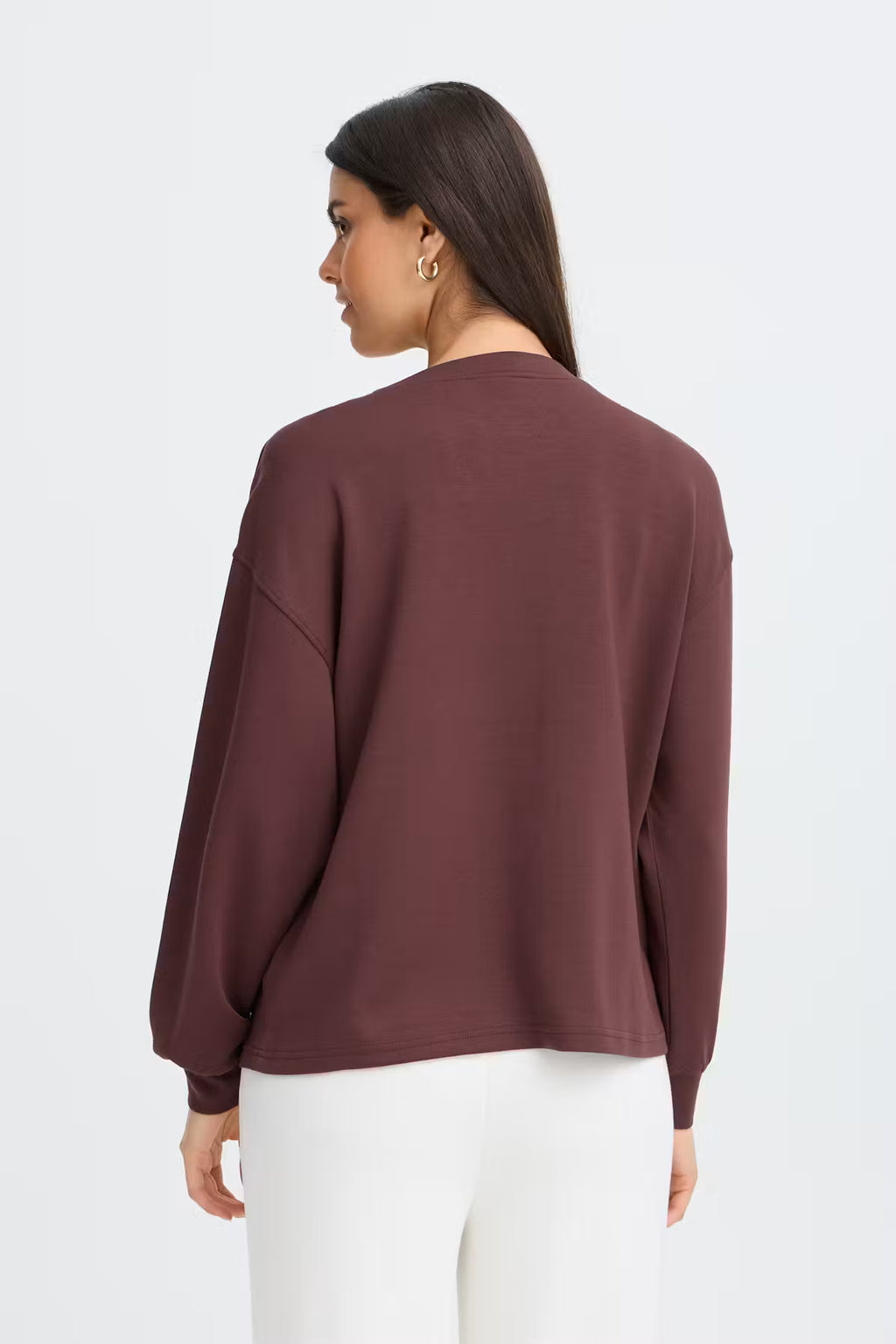 A woman shown from the back wearing a FRAURORA PU 7 Sweatshirt in Rum Raisin/Red  and white pants, against a plain light gray studio background.
