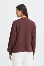 A woman shown from the back wearing a FRAURORA PU 7 Sweatshirt in Rum Raisin/Red  and white pants, against a plain light gray studio background.