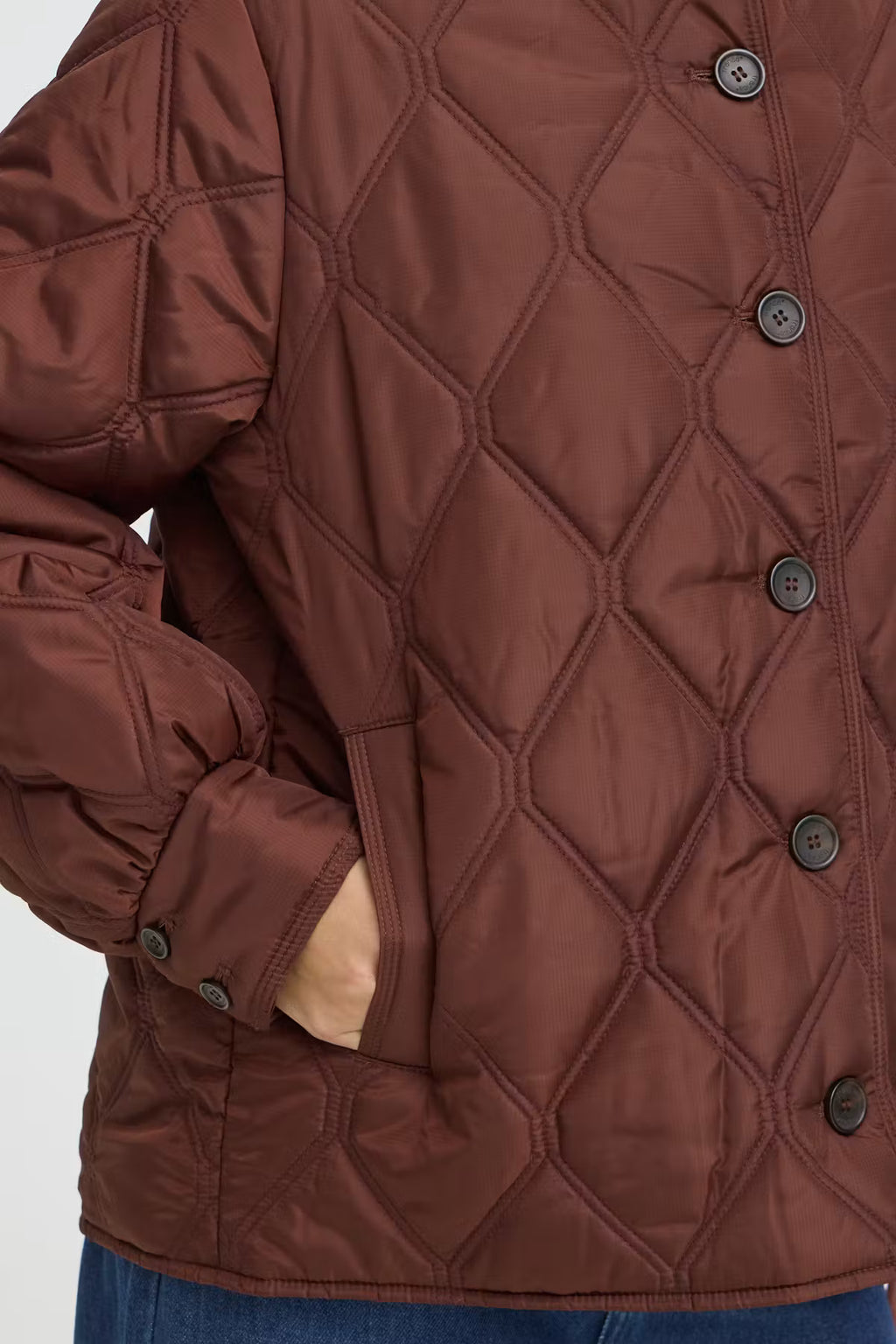 Close-up of a FRAGATE Outerwear in Rum Raisin/Red with dark buttons, showing part of a person's hand in a pocket and blue jeans at the bottom.