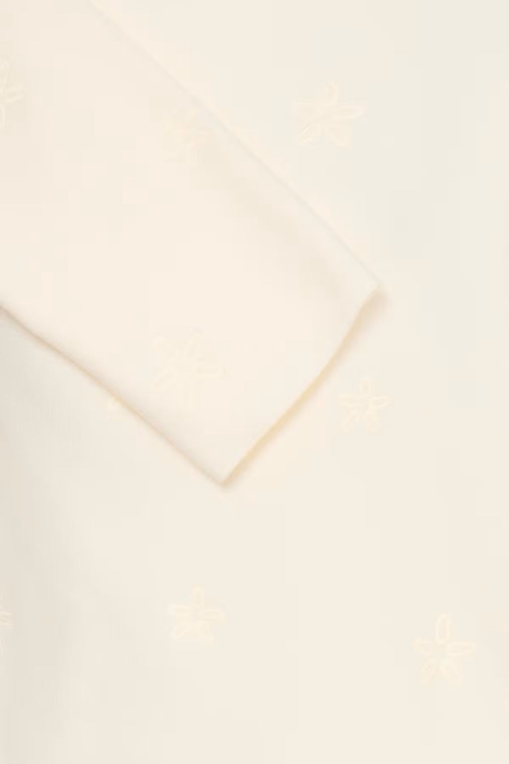 A close-up of a Whisper White pullover with a subtle tonal embroidered pattern .