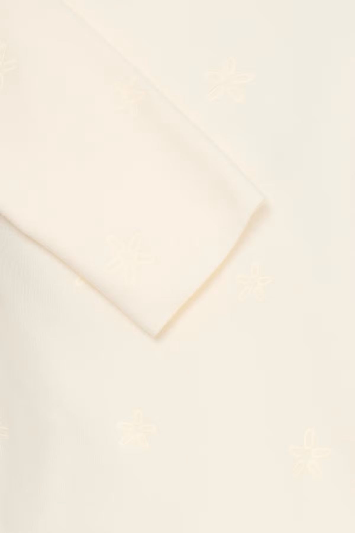 A close-up of a Whisper White pullover with a subtle tonal embroidered pattern .