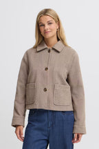 A woman modeling a cropped FREVILLA Outerwear in Rain-Drum Mix/Brown, three front buttons, and two large front patch pockets, paired with blue jeans against a light gray studio background.