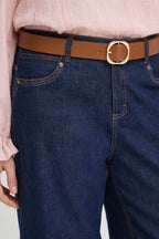 A close-up of a person wearing dark blue denim jeans, a tan leather belt with a gold-tone buckle, and a light pink blouse.
