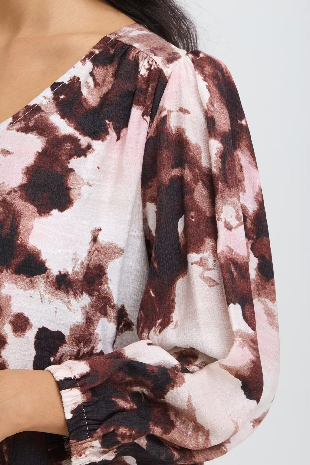 Close-up of a woman wearing Watercolour Bloom Rum Raisin / Red a long-sleeve blouse. The blouse features a gathered neckline and voluminous sleeves.