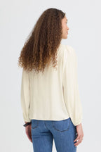 Person wearing a Whisper White blouse and blue jeans on a white background