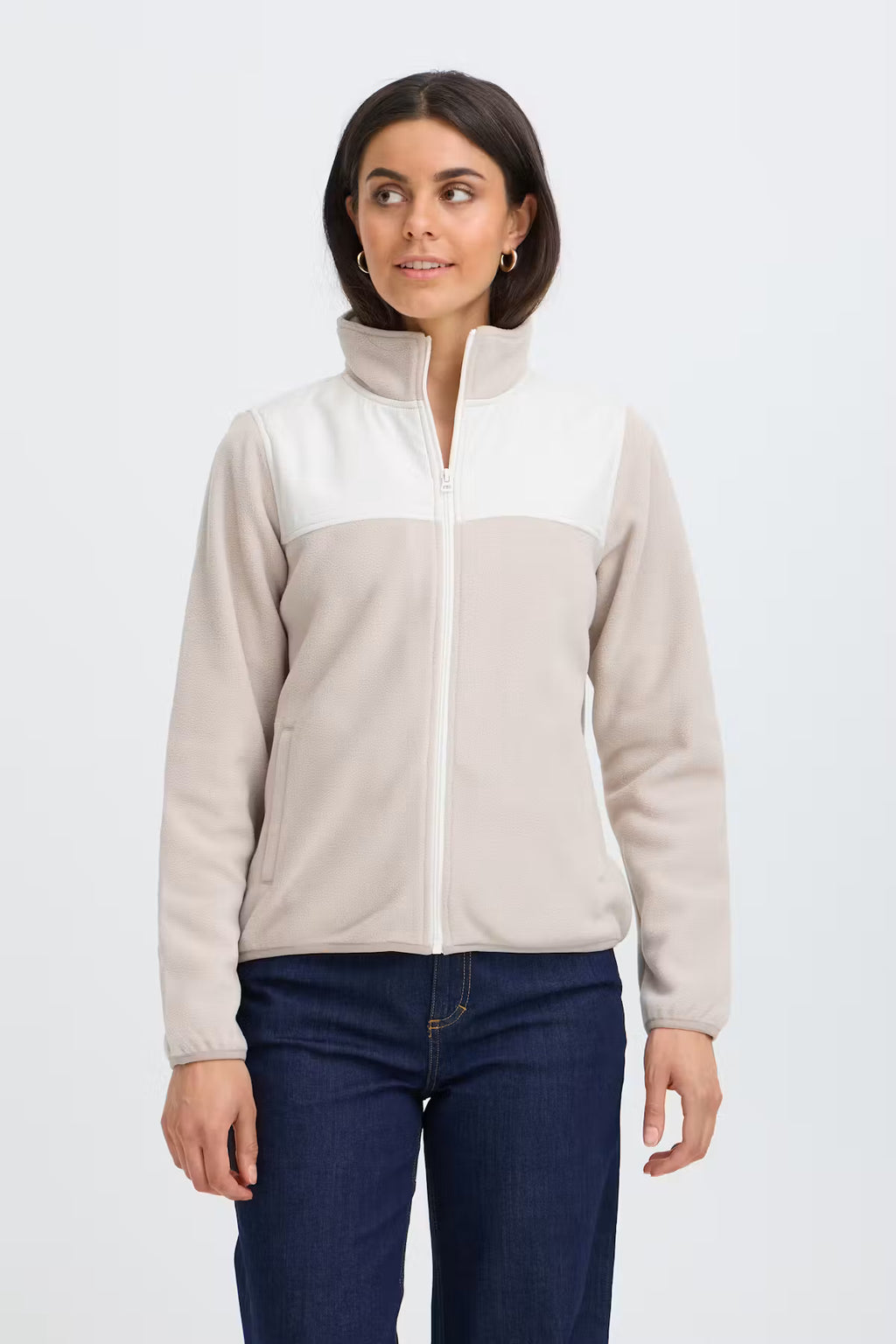 A woman modeling a cFRFLEA Outerwear in String/Nature with a white upper panel and collar, and a light beige lower body and sleeves, paired with dark blue jeans against a light gray studio background.