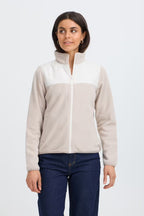 A woman modeling a cFRFLEA Outerwear in String/Nature with a white upper panel and collar, and a light beige lower body and sleeves, paired with dark blue jeans against a light gray studio background.