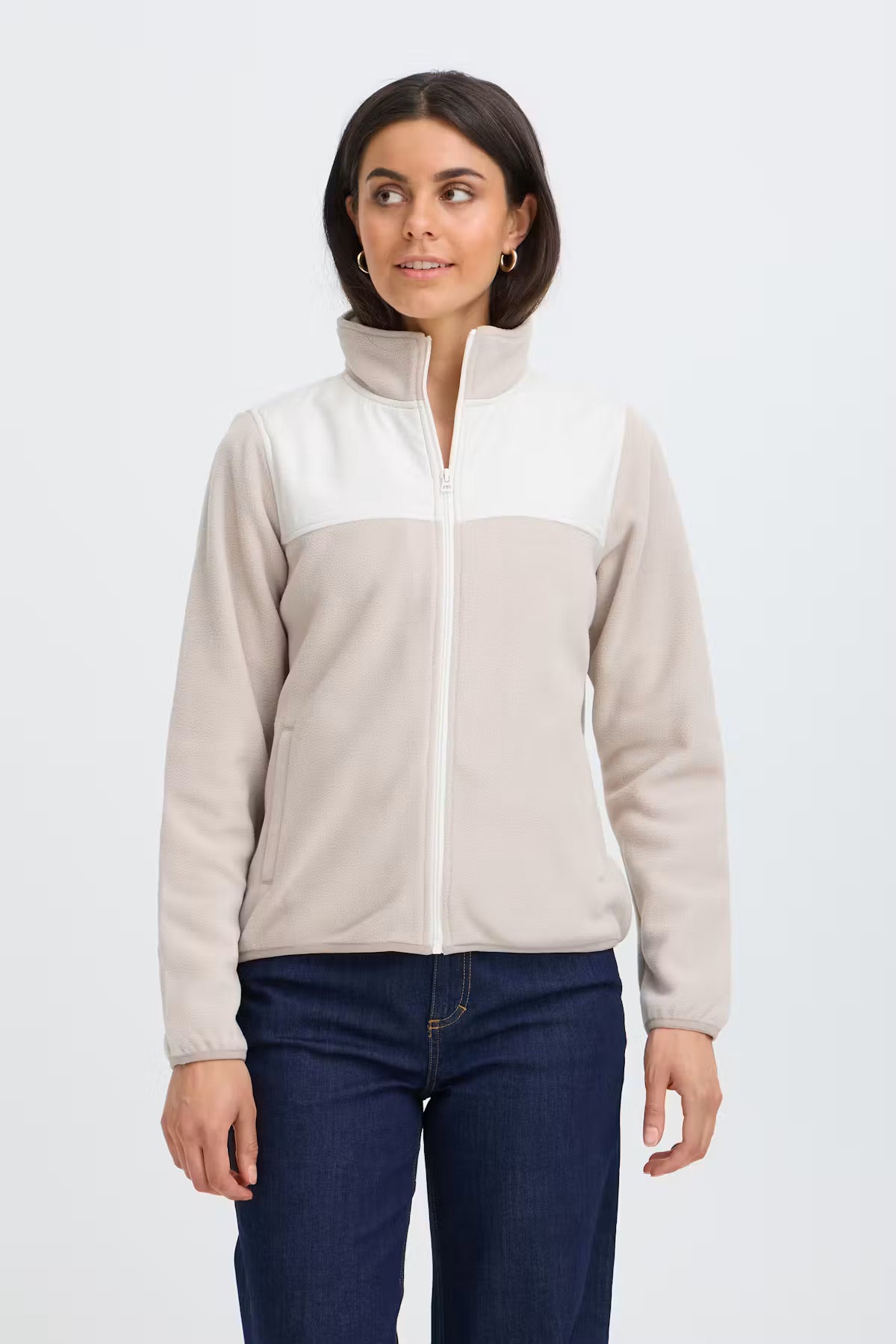 A woman modeling a cFRFLEA Outerwear in String/Nature with a white upper panel and collar, and a light beige lower body and sleeves, paired with dark blue jeans against a light gray studio background.