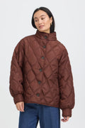 A woman wearing a bFRAGATE Outerwear in Rum Raisin/Red with a high stand collar and dark buttons, paired with blue jeans, against a light gray studio background.