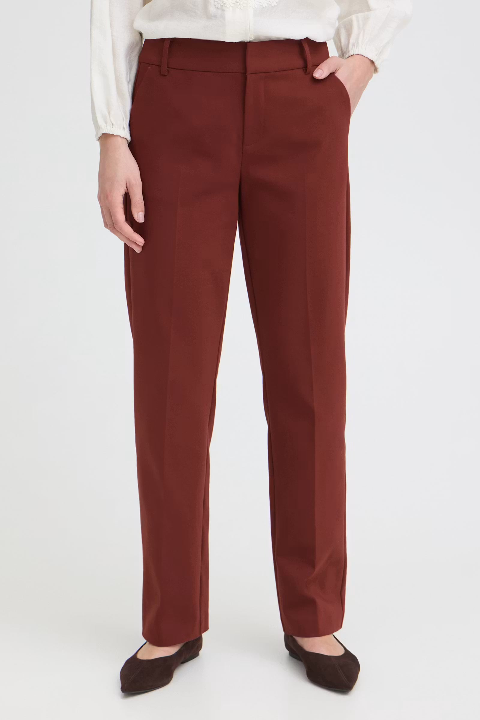 A person wearing straight-leg 
Rum Raisin / Red, paired with a white blouse and dark brown flats, shown from the waist down against a light gray studio background.