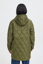 A person shown from the back wearing a quilted hooded jacket in FRAGATE Outerwear in Grape Leaf/Green, paired with blue jeans, against a plain light gray studio background.