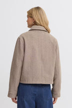 A woman shown from the back wearing a cropped FREVILLA Outerwear in Rain-Drum Mix/Brown and blue jeans against a plain light gray studio background.