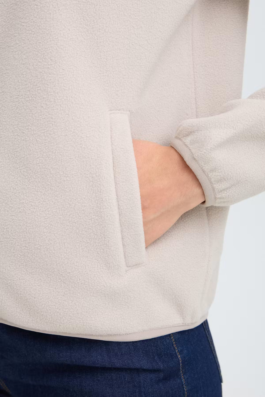 Close-up of a person wearing FRFLEA Outerwear in String/Nature with a side pocket, showing the fabric texture and a hand in the pocket, paired with dark blue jeans.