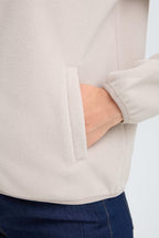 Close-up of a person wearing FRFLEA Outerwear in String/Nature with a side pocket, showing the fabric texture and a hand in the pocket, paired with dark blue jeans.