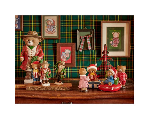 Collection of teddy bears in festive attire against a plaid wall with framed pictures.