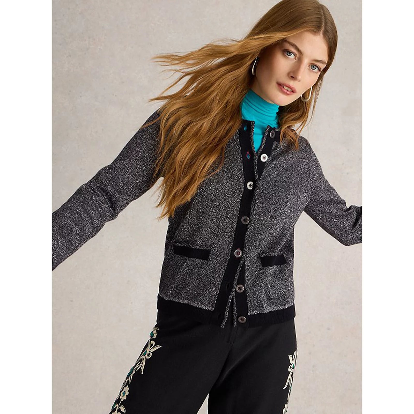 Woman wearing a gray cardigan over a black outfit with a light background