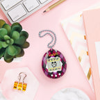 Colorful Tamagotchi-style device on a pink surface with stationery items
