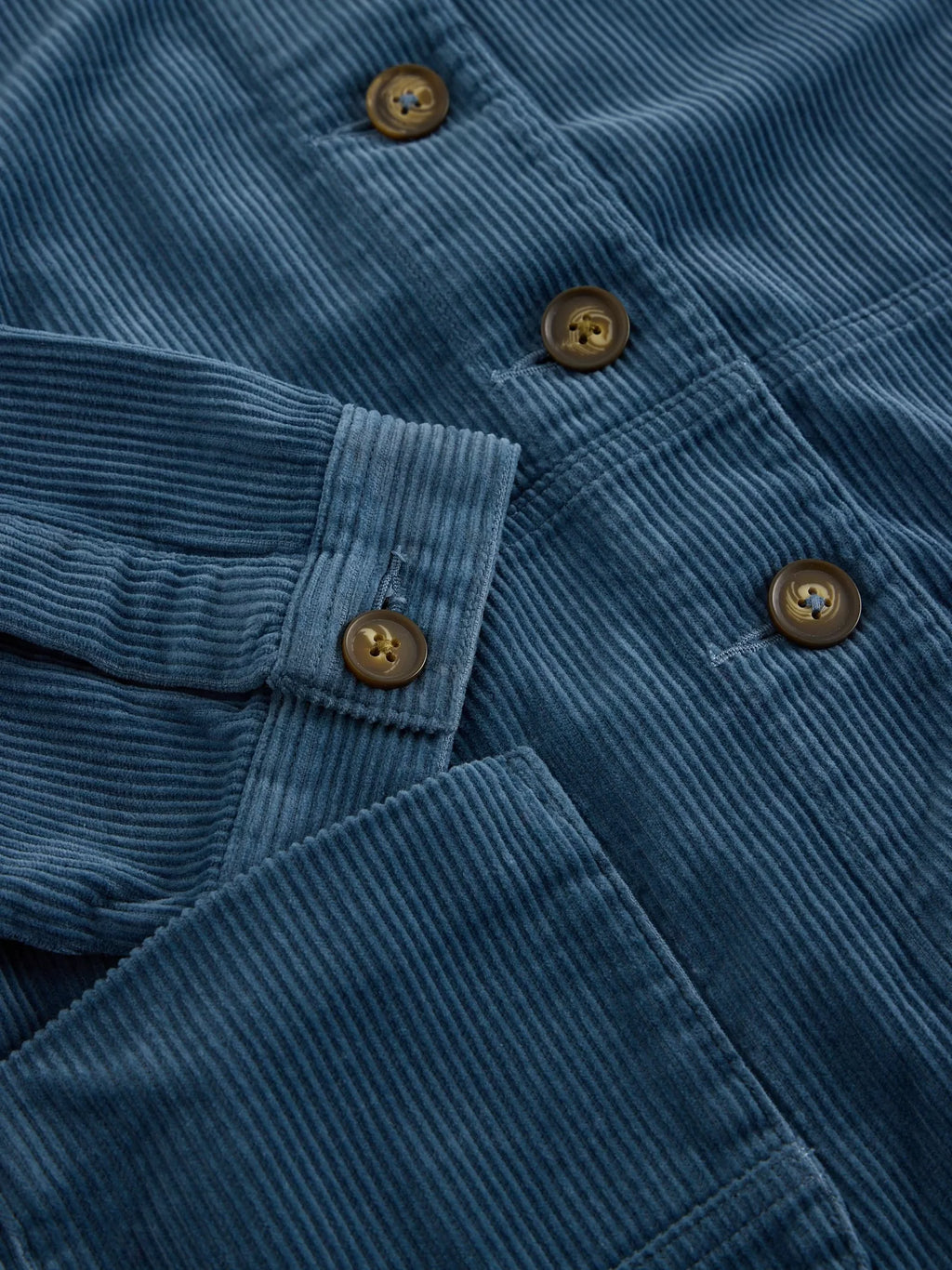 Close-up of a blue corduroy button-up shirt showing the ribbed texture, pocket detail, and brown buttons.