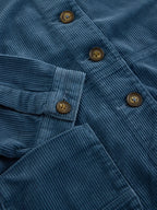 Close-up of a blue corduroy button-up shirt showing the ribbed texture, pocket detail, and brown buttons.