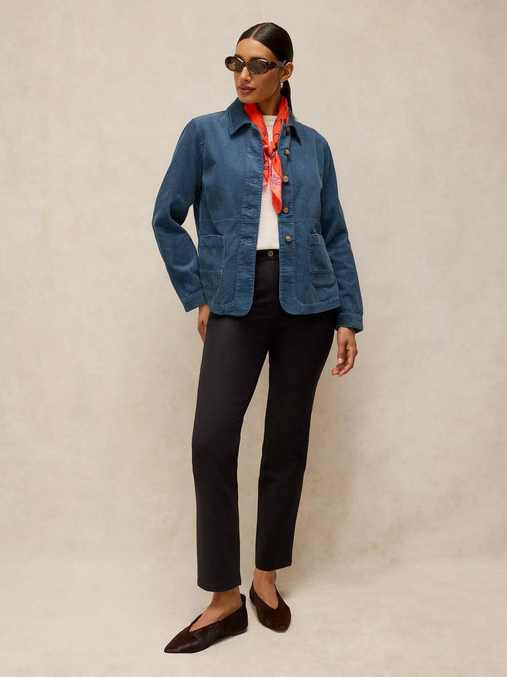 Person wearing a blue jacket, black pants, and sunglasses on a beige background