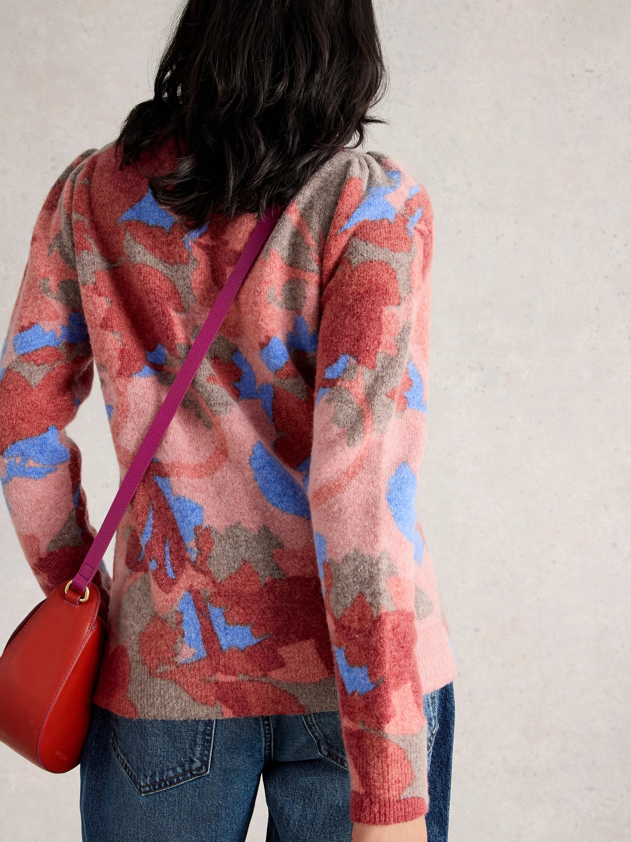Person wearing a colorful sweater with a red bag on a plain background