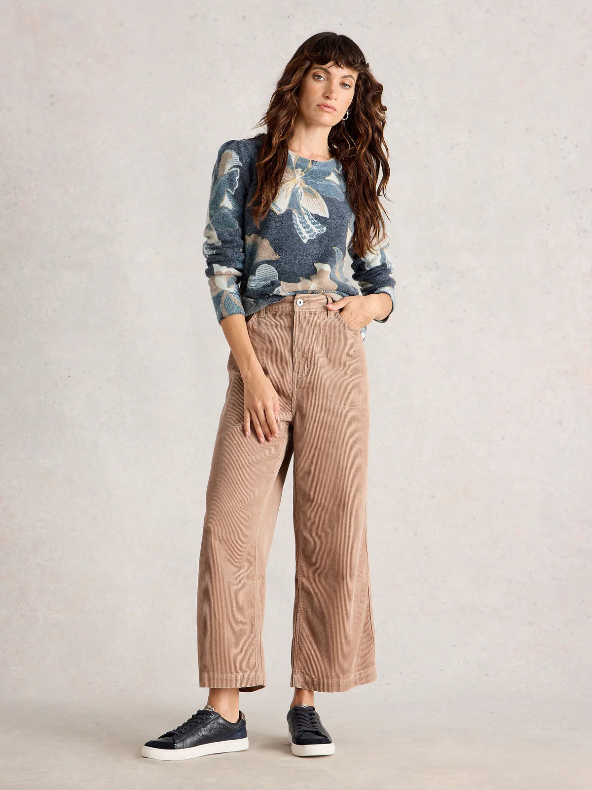 Woman wearing a floral sweater and beige pants against a plain background