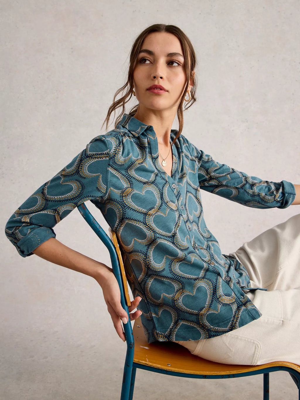 Woman wearing a blue patterned shirt sitting on a chair against a plain background