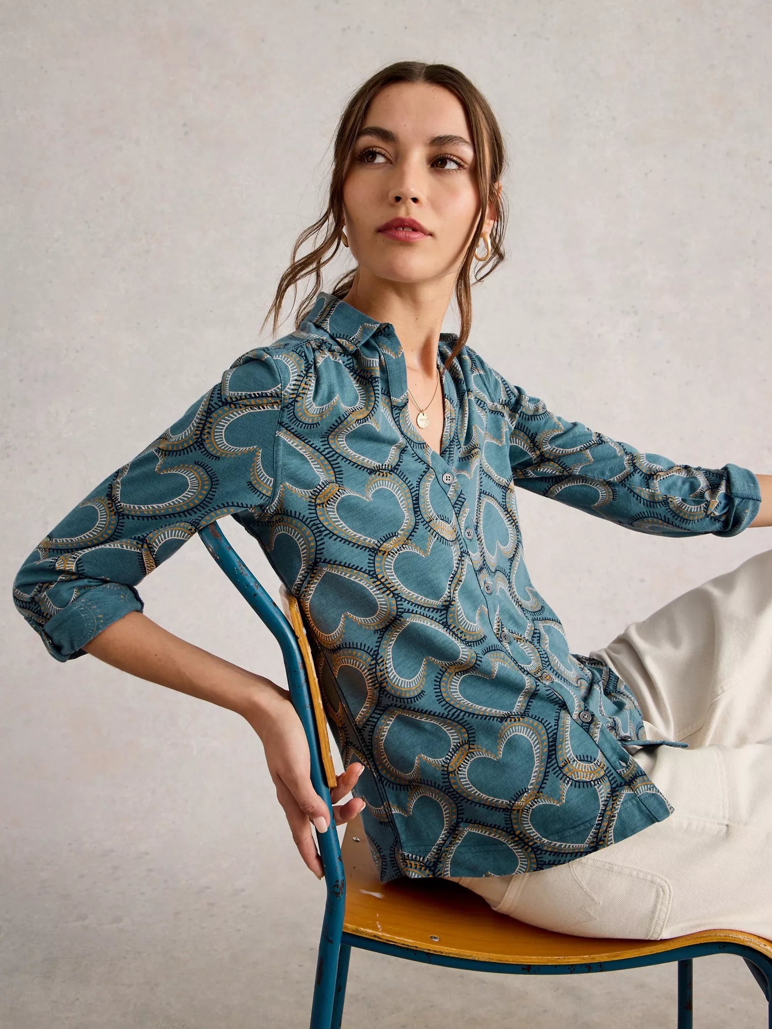 Woman wearing a blue patterned shirt sitting on a chair against a plain background