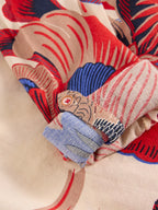 Close-up of a fabric with red, blue, and beige patterns on a beige background