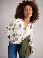 Woman wearing a patterned shirt and holding a green bag against a gray background