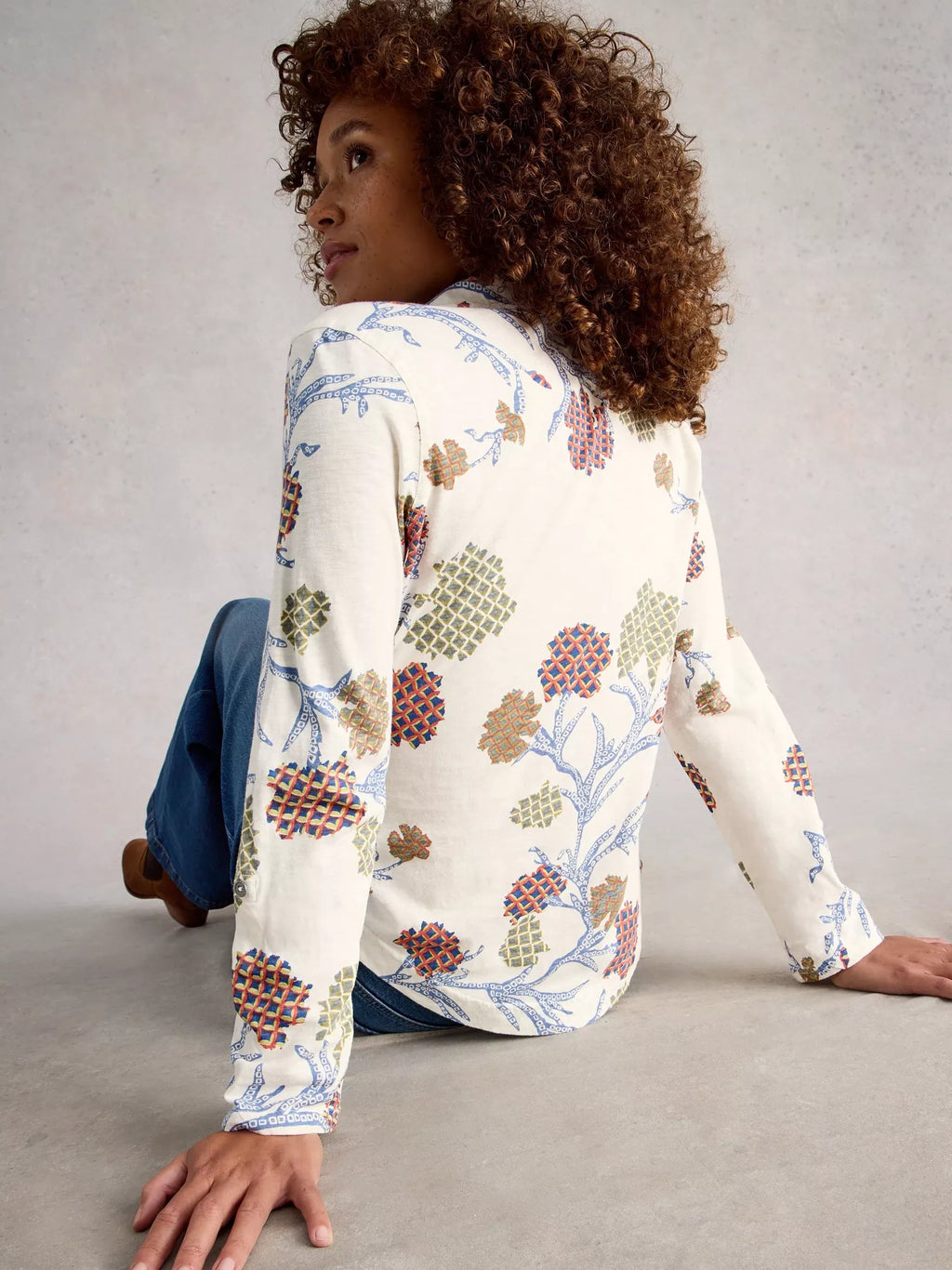 Woman wearing a floral patterned shirt sitting on the floor against a plain background