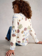 Woman wearing a floral patterned shirt sitting on the floor against a plain background