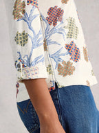 Close-up of a person wearing a patterned shirt with blue jeans on a light gray background