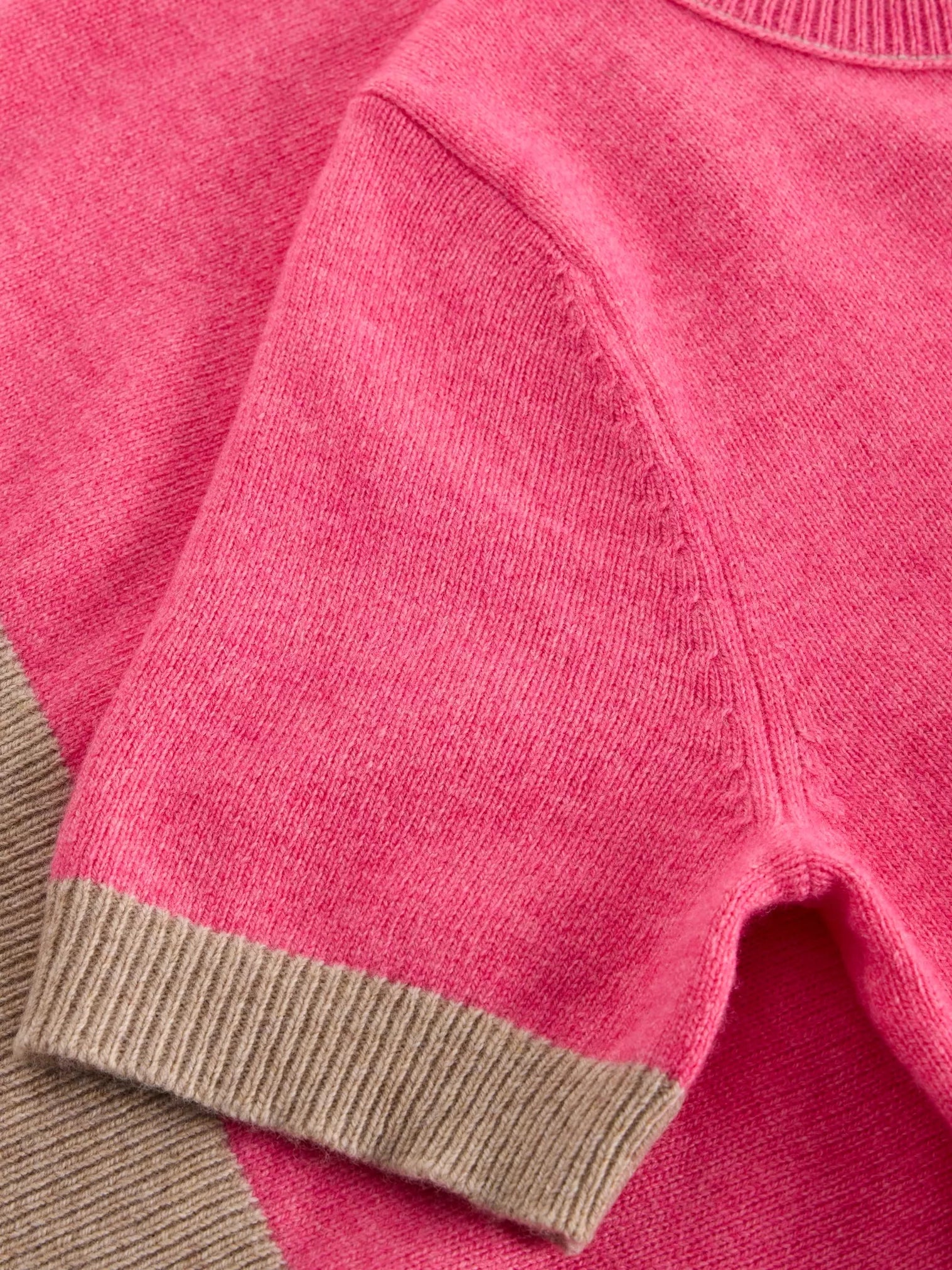 Close-up of a pink sweater with brown trim on a matching pink background