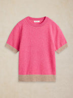 A short-sleeve crewneck knit sweater in bright pink with contrasting beige ribbed trim at the cuffs and hem, displayed flat against a neutral beige background.