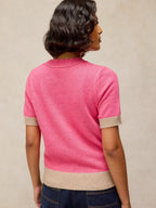 Person wearing a pink sweater with beige trim on a neutral background