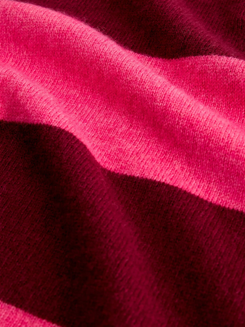 A close-up of a soft knit fabric with draped folds in bright pink and deep burgundy.
