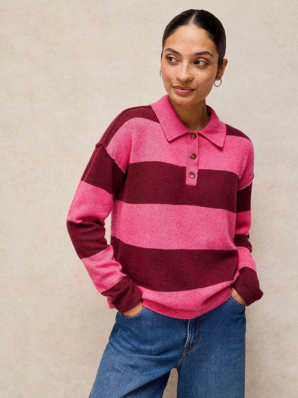 Person wearing a pink and burgundy striped sweater with a plain background