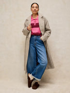 Woman wearing a long coat, pink shirt, and blue jeans against a plain background