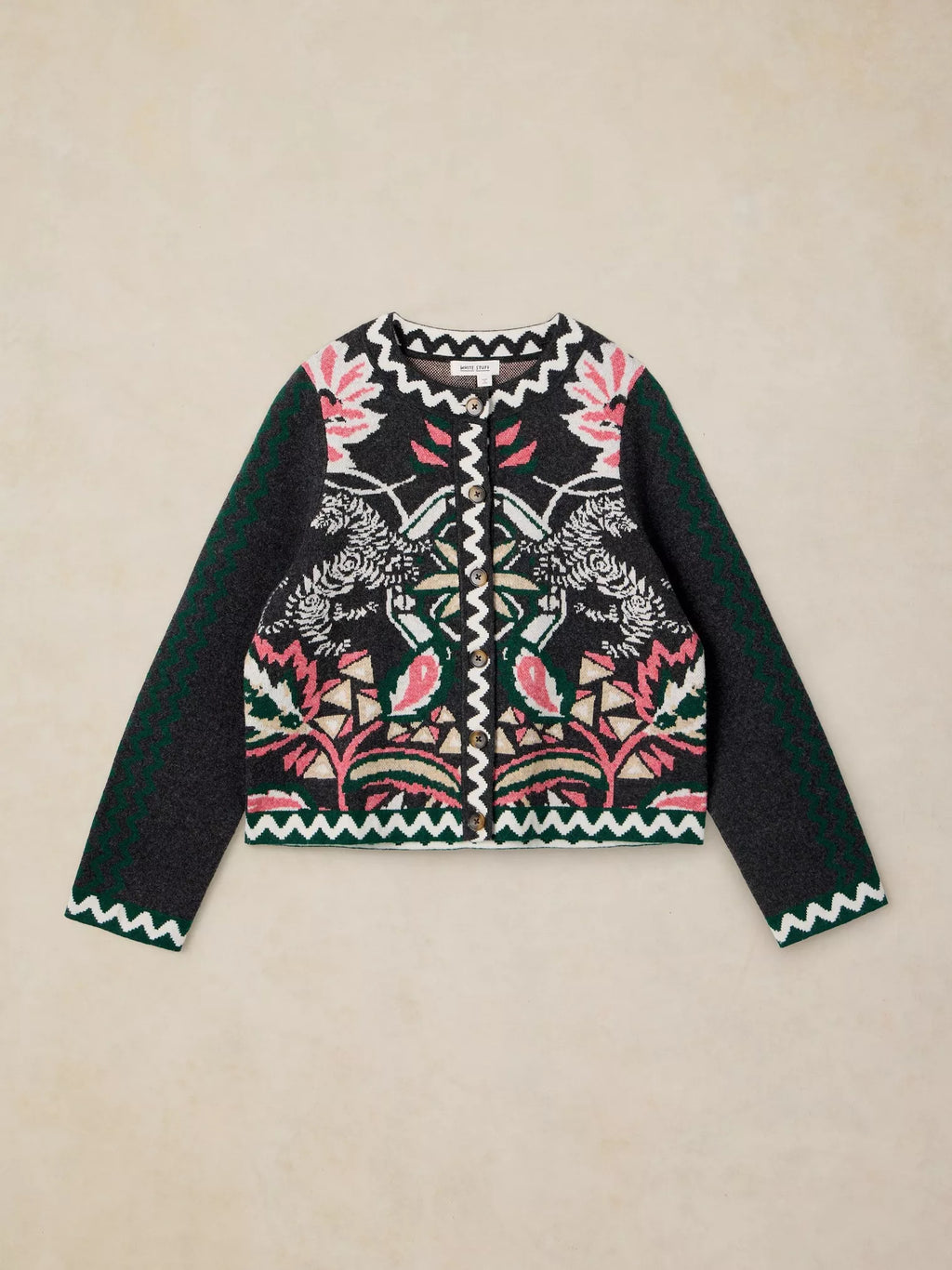 A cropped knit cardigan sweater featuring a black base with a colorful embroidered pattern of birds, leaves, and geometric motifs, with solid dark green sleeves and zigzag trim, laid flat on a beige background.