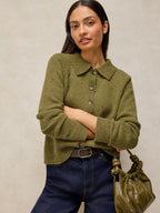 A woman wearing Shepherd Collar Cardi – Mid Chartreuse paired with dark blue jeans and holding an olive green handbag, set against a neutral textured beige background.